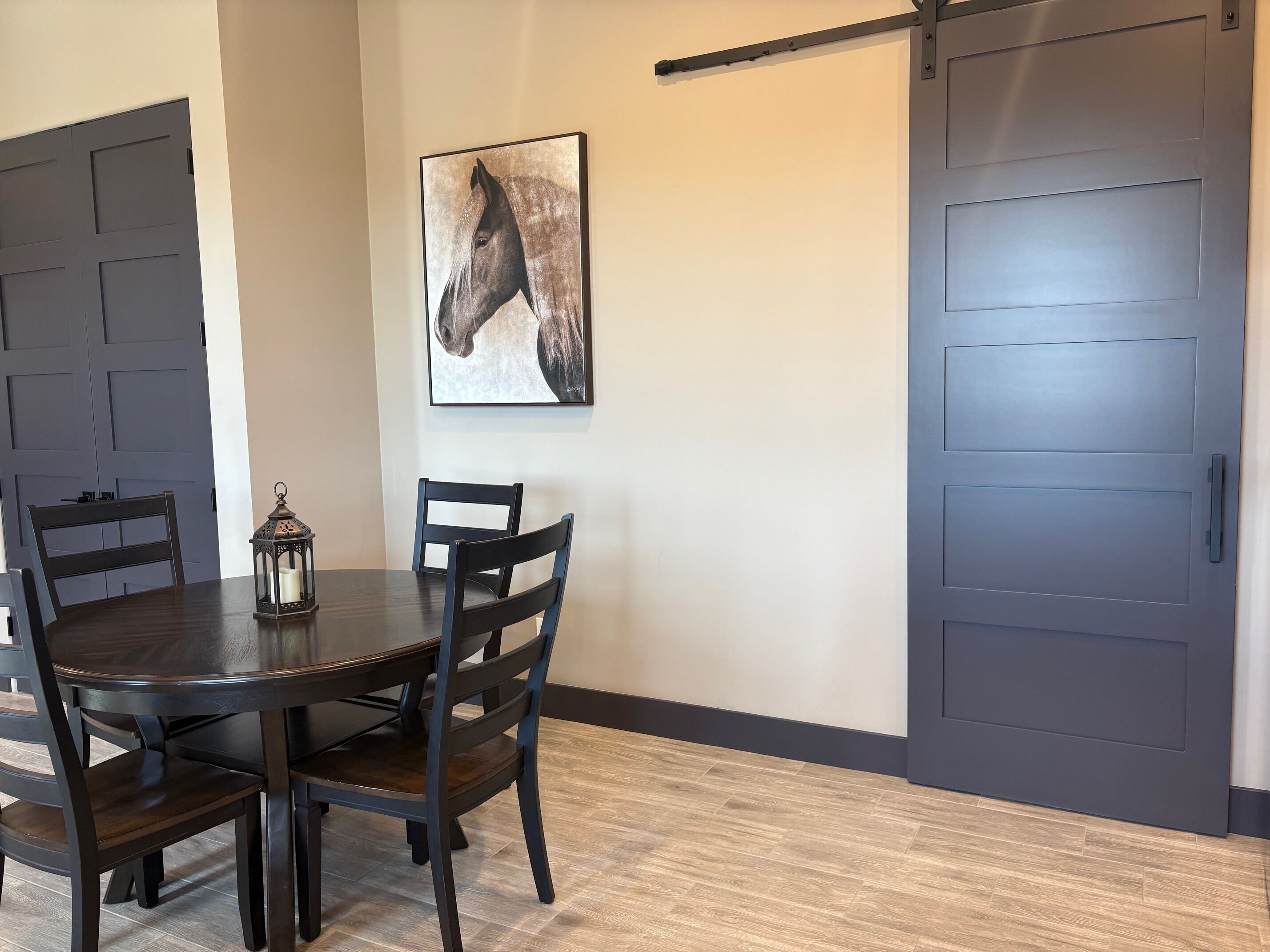 Uma sala de jantar com uma mesa de madeira escura, cadeiras, um candeeiro e um quadro de um cavalo na parede.