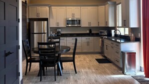 Una cocina moderna con comedor, que presenta armarios de colores claros, electrodomésticos de acero inoxidable y una mesa de comedor de madera oscura.