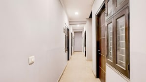 Een gang met deuren aan beide kanten, een lichtschakelaar aan de linker muur en een vloerbedekking.