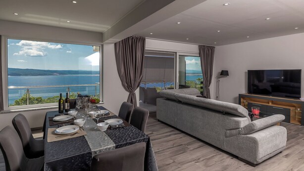 A modern living room with a large TV, a sofa, and a dining area with a table set for two. - Beautiful modern 4 star apartment with sea view (Dramalj)