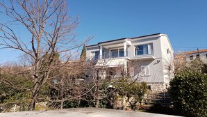 A two-story building with a balcony, surrounded by trees and vegetation. - Beautiful modern 4 star apartment with sea view (Dramalj)