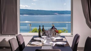 A dining table set with plates, glasses, and wine bottles, overlooking a scenic view of a body of water and distant land. - Beautiful modern 4 star apartment with sea view (Dramalj)