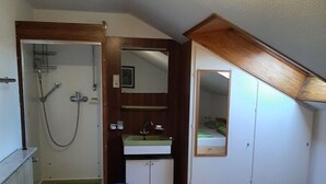 Apartamento pequeno e individual, com chuveiro, pia, cama e espelho.