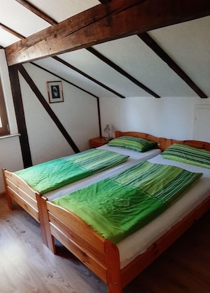A single wooden bed with green bedding in a room with exposed wooden beams and a small bedside table.