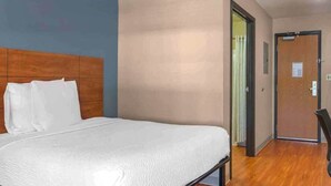 Habitación de hotel con cama, cabecera de madera, una puerta y pared con interruptor de luz.
