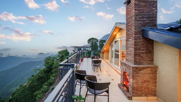A balcony with chairs, a brick fireplace, and a view of the mountains. - Konifer Villas By ELIVAAS (Kasauli)