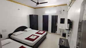 A hotel room with two beds, a ceiling fan, an air conditioning unit, a sink, and a mirror. - Hotel Gananjaya Gokarna (Gokarna)