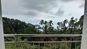 A balcony with a metal railing, a tiled floor, and a view of dense greenery and palm trees. - Hotel Gananjaya Gokarna (Gokarna)