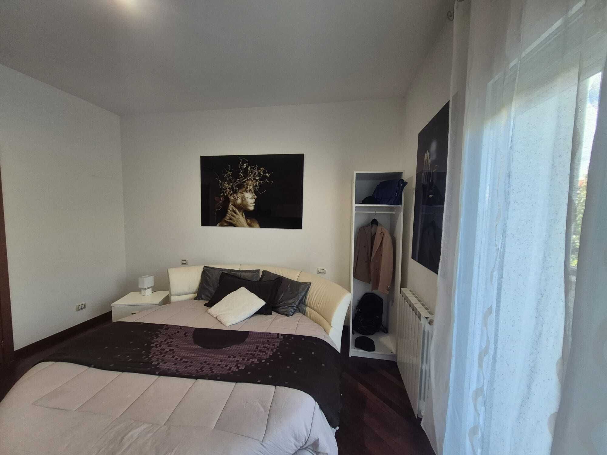 Een slaapkamer met een bed, nachtkastje, garderobe en een schilderij aan de muur.