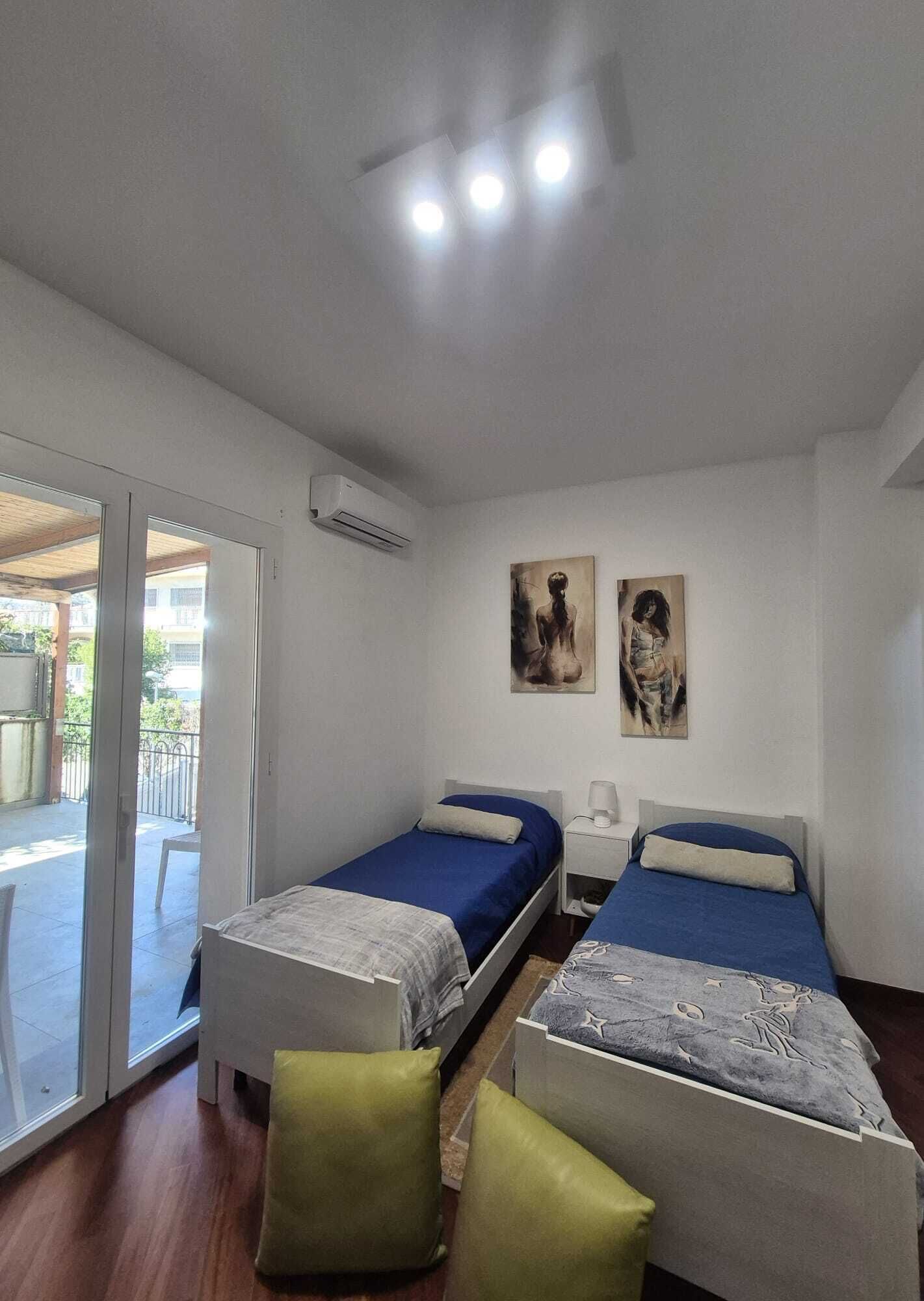 Une chambre avec deux lits, un ventilateur de plafond, un appareil de climatisation et deux œuvres d’art accrochées au mur.