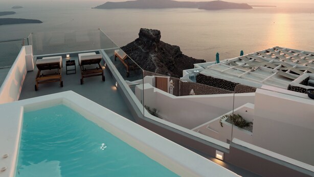 Une piscine à débordement située sur le toit, avec des chaises longues et une vue sur la mer au coucher du soleil.