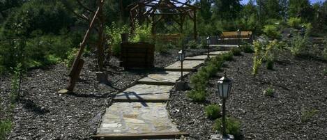 A stone pathway leading to a wooden gazebo surrounded by greenery.