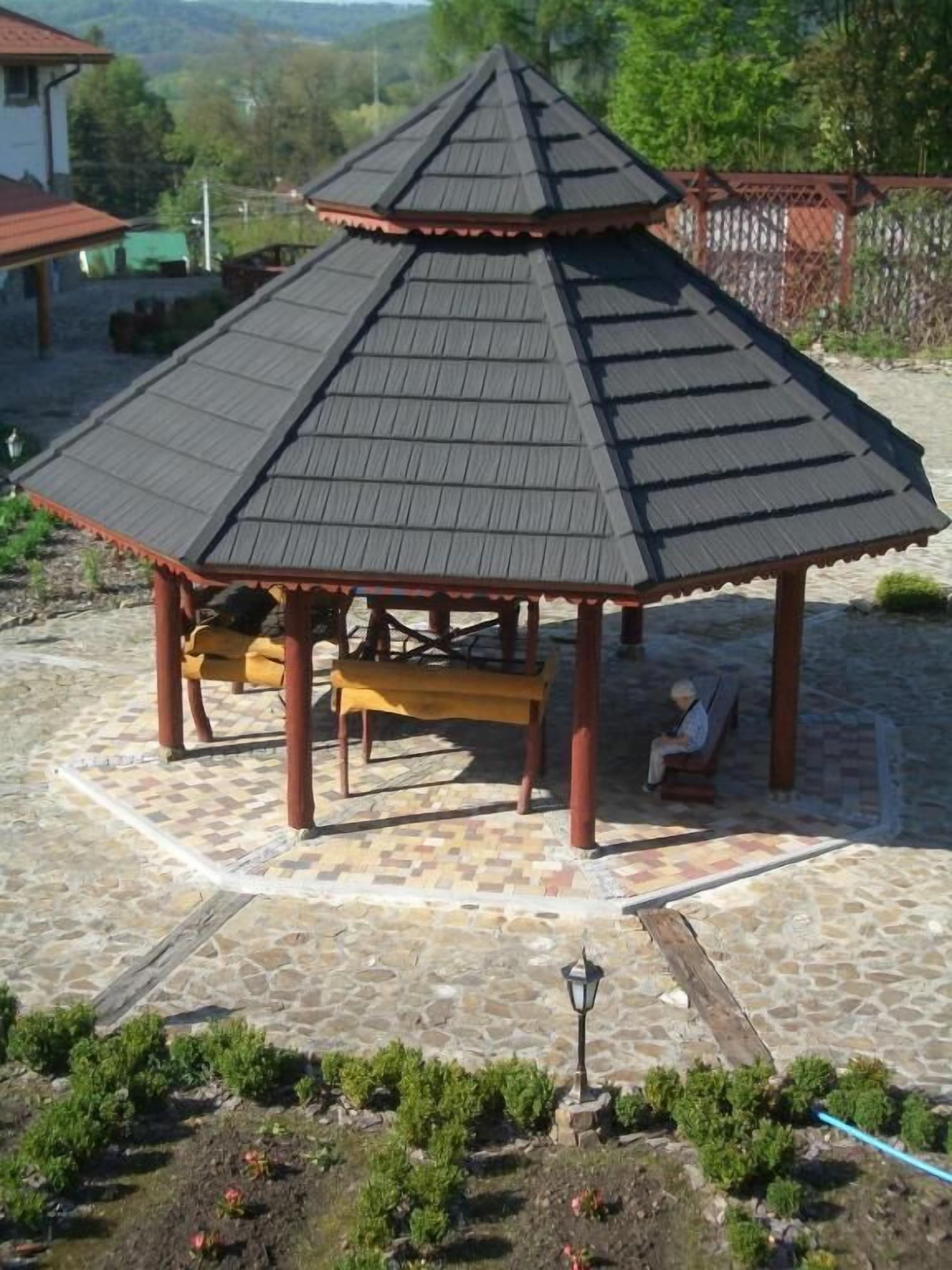A gazebo with a tiled floor and benches, surrounded by a stone patio.