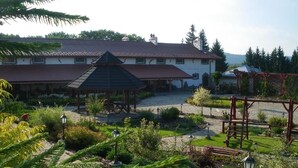 A building with a covered patio area, a garden with various plants, and a wooden structure. - Impresja Krasiczyn (Krasiczyn)