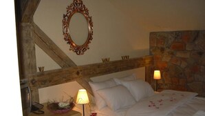 A bedroom with a bed, a nightstand with a lamp, a wooden headboard, a stone wall, and a mirror on the ceiling. - Impresja Krasiczyn (Krasiczyn)