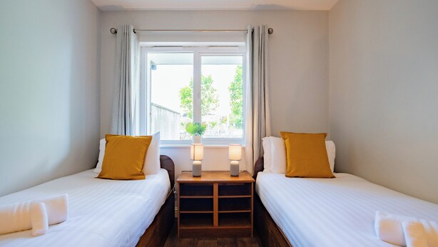 Une chambre double avec deux lits, une petite table avec des lampes, une fenêtre avec des rideaux et une plante sur le rebord de la fenêtre.