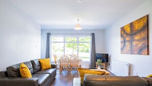 Un salon moderne avec un canapé, une table basse et un téléviseur. On y trouve également une table à manger avec des chaises, ainsi qu’une fenêtre avec des rideaux.