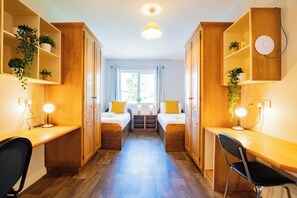 Ein Zimmer mit zwei Betten, einem Schreibtisch und Regalen mit Pflanzen.