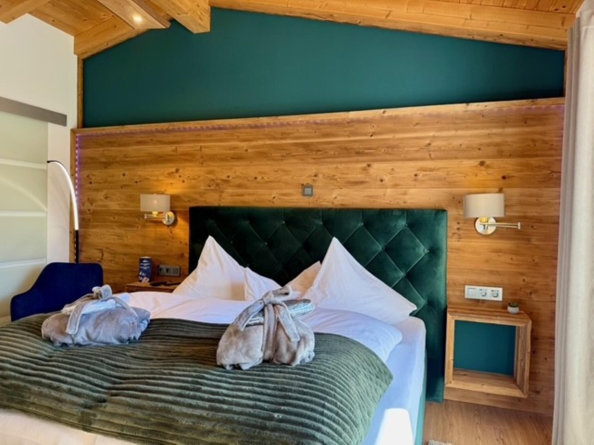 Een kamer met houten lambrisering, een bed, kussens, een groen hoofdeinde en wandlampen.