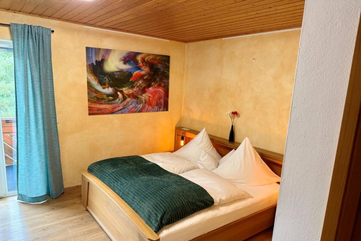 Een slaapkamer met een houten bed, een schilderij aan de muur en een raam met gordijnen.