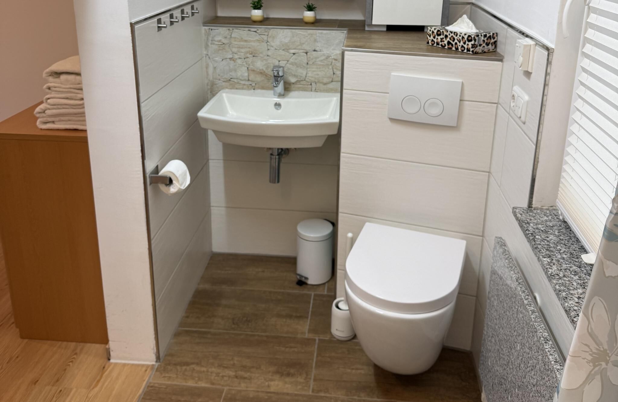 A compact bathroom with a sink, toilet, and a small trash bin.