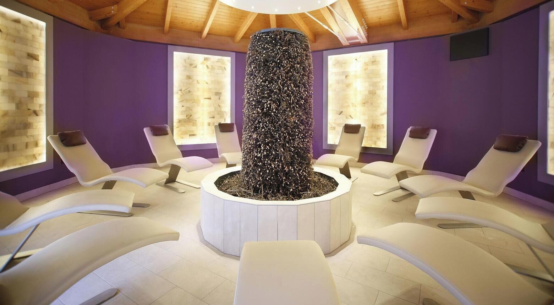 A spa room with white chairs arranged around a central pillar, wooden ceiling beams, and purple walls.