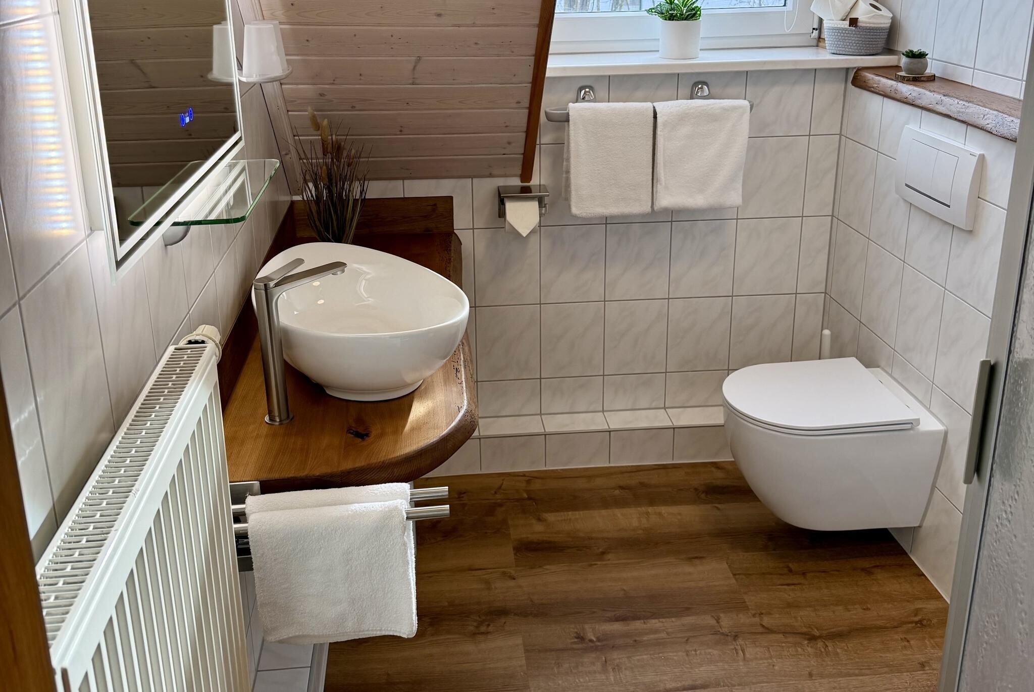 A modern bathroom with a wooden vanity, white sink, and toilet.