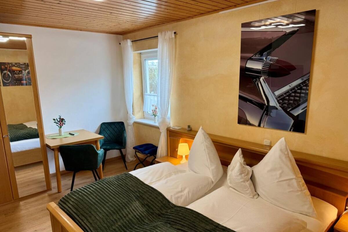 Een hotelkamer met een bed, een bureau, een stoel, een raam met gordijnen, een lamp en een poster aan de muur.