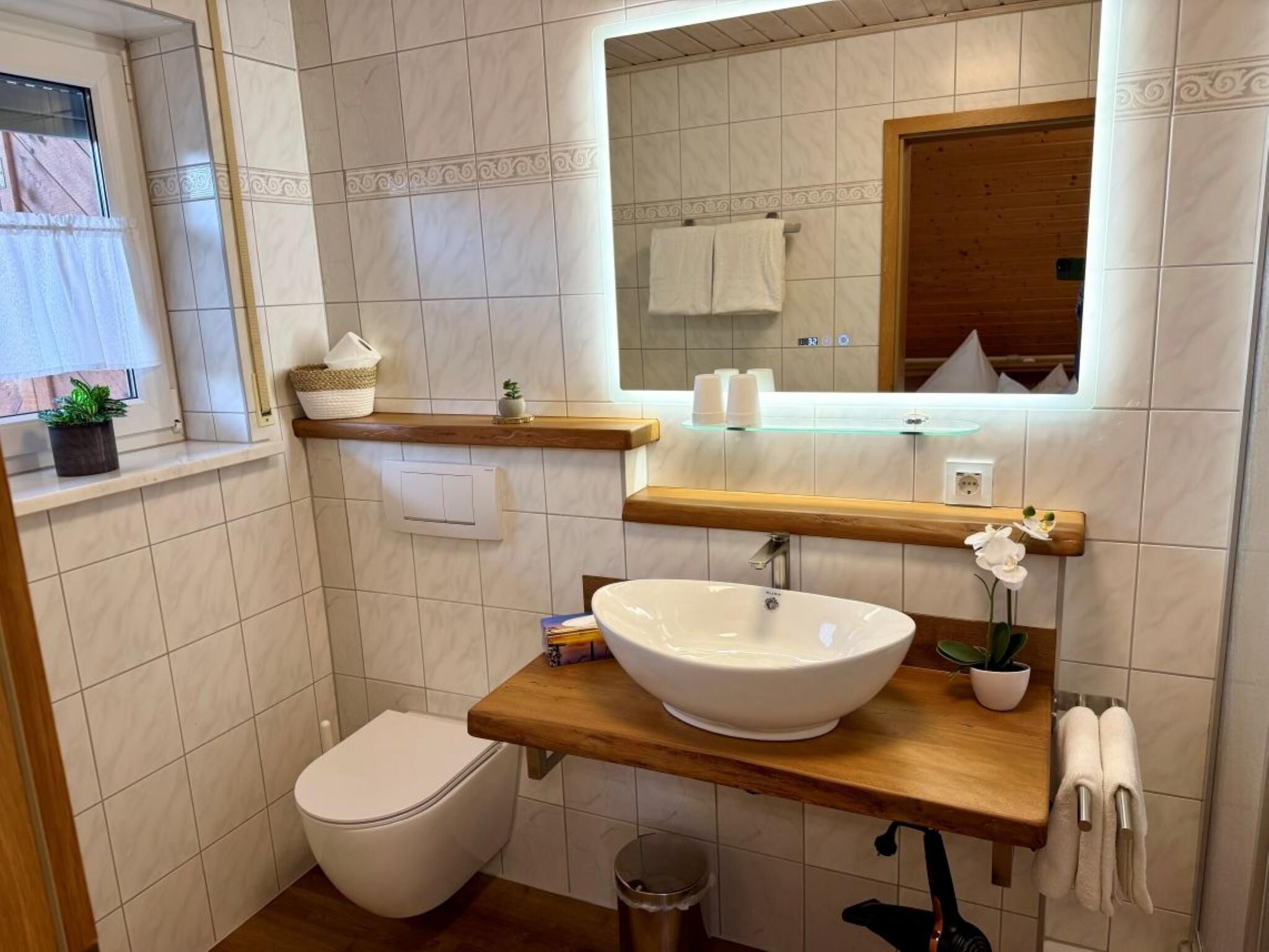 Ein modernes Badezimmer mit Toilette, großem Spiegel, Holzwaschtisch mit Spüle und einer kleinen Topfpflanze.