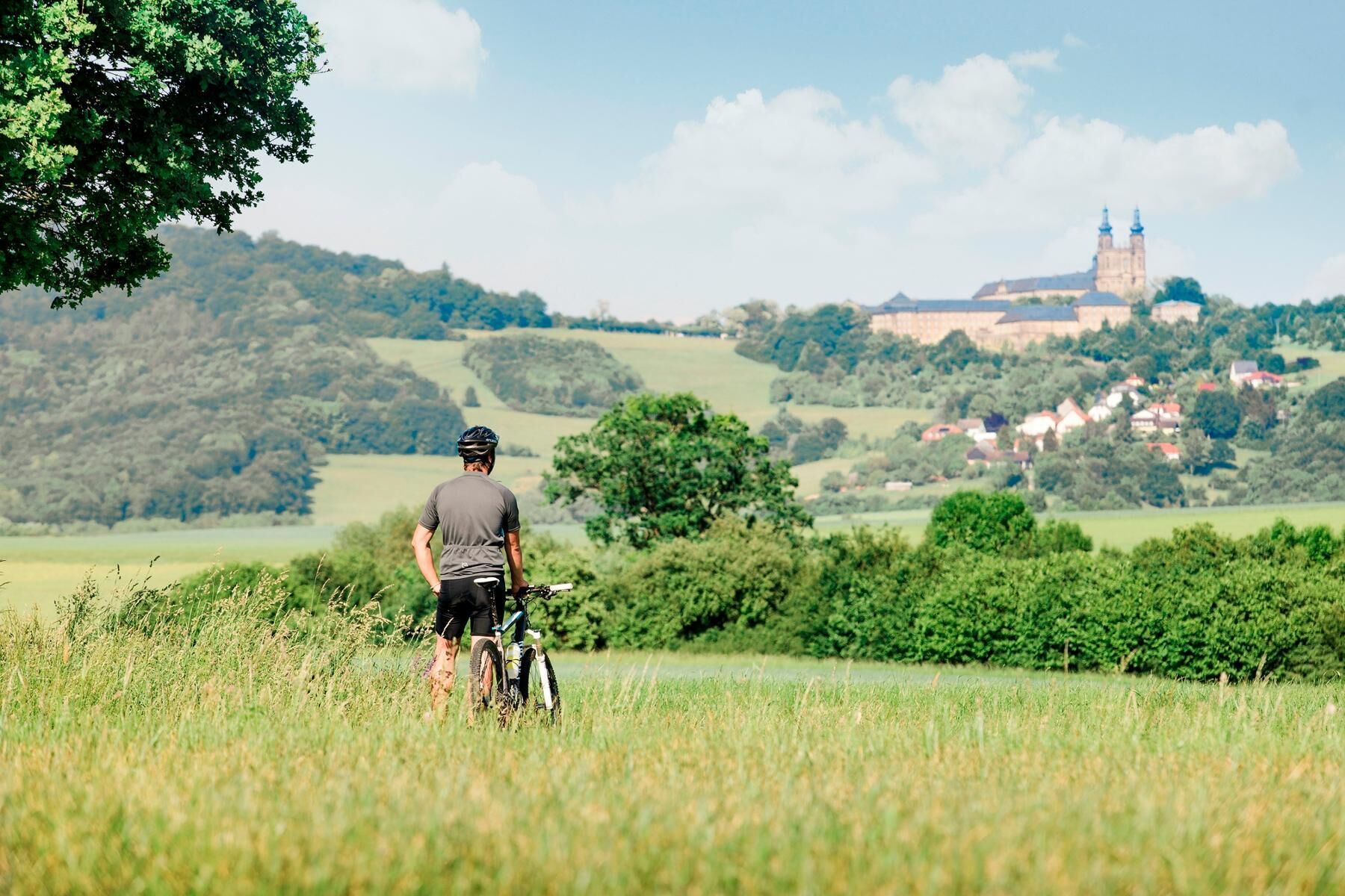 Un ciclista en un campo de hierba, con un edificio histórico al fondo.