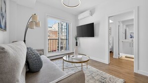 Een moderne woonkamer met een bank, een ronde salontafel, een vloerlamp, een televisie en een schuifdeur die leidt naar een buitenruimte.