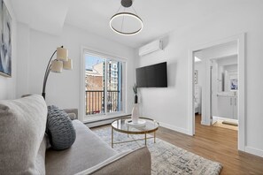 A modern living room with a sofa, a round coffee table, a floor lamp, a TV, and a sliding glass door leading to an outdoor area. - 2BR | Downtown | AC | Mins to Saddledome (Calgary)