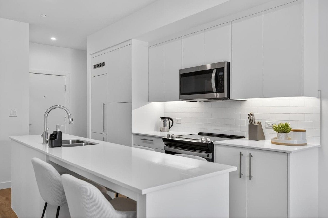 A modern kitchen with white cabinetry, a stainless steel microwave, and a built-in oven.