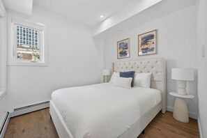 A bedroom with a large bed, two bedside tables, a window, and artwork on the wall. - 2BR | Downtown | AC | Mins to Saddledome (Calgary)