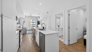 Een moderne keuken met een centraal eiland, een eethoek met stoelen en uitzicht op een balkon.