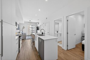 A modern kitchen with a central island, a dining area with chairs, and a view of a balcony. - 2BR | Downtown | AC | Mins to Saddledome (Calgary)