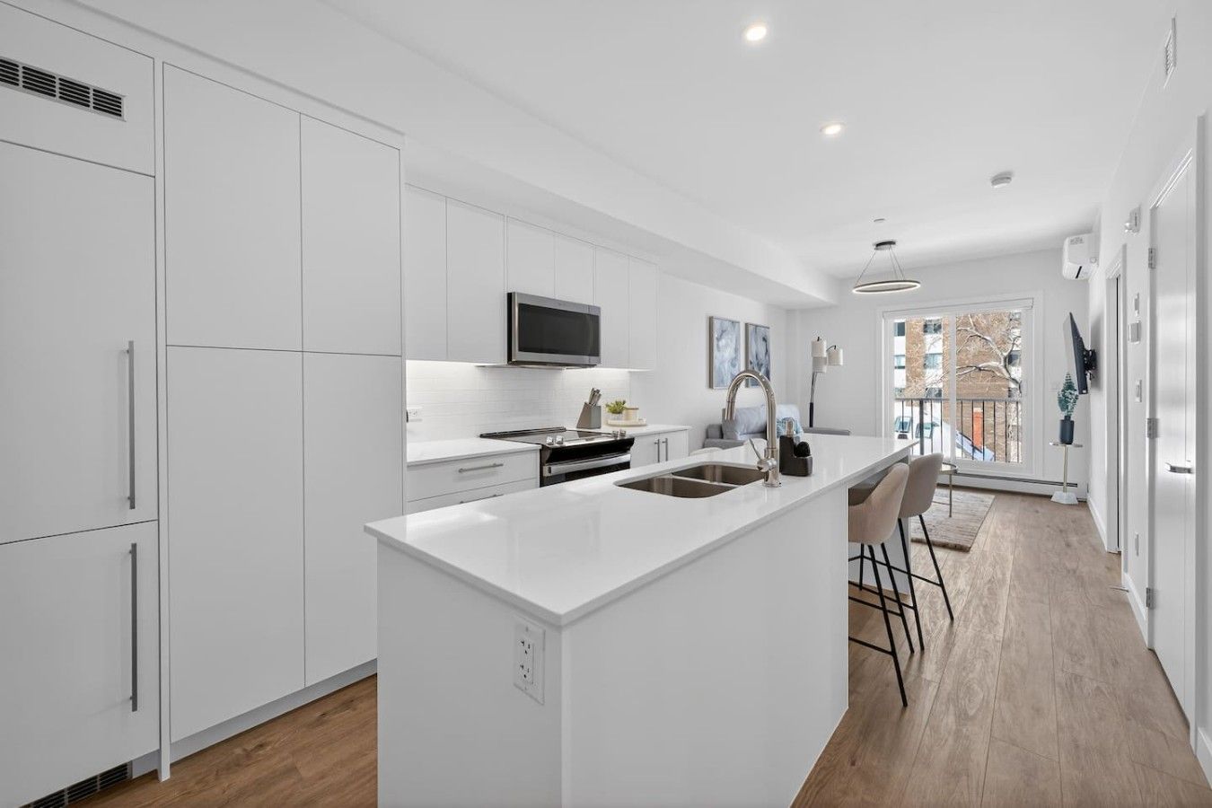 A modern kitchen with white cabinetry, a central island with a sink, and a large window providing a view of the outdoors.