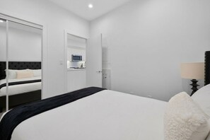 Ein Hotelzimmer mit Bett, Nachttisch, Lampe, Kleiderschrank und einer Tür zu einem Badezimmer.
