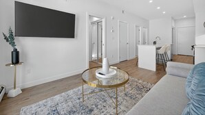 Een moderne woonkamer met een televisie, een ronde salontafel, een bank en een keuken op de achtergrond.