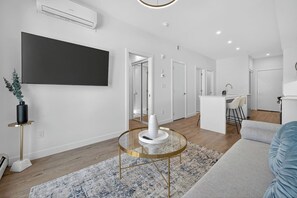A modern living room with a TV, a round coffee table, a sofa, and a kitchen area in the background. - 2BR | Downtown | AC | Mins to Saddledome (Calgary)