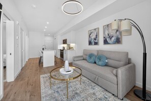 A modern living room with a grey sofa, round coffee table, and artwork on the wall. - 2BR | Downtown | AC | Mins to Saddledome (Calgary)