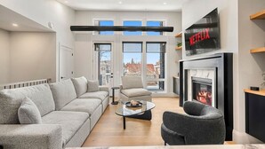 A modern living room with a sofa, armchair, coffee table, fireplace, and a TV mounted on the wall. - Ember House | Lux 2 Bed | Min to DT (Calgary)