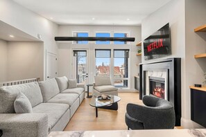 A modern living room with a sofa, armchair, coffee table, fireplace, and a TV mounted on the wall. - Ember House | Lux 2 Bed | Min to DT (Calgary)