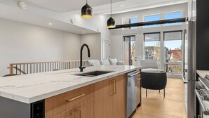 A modern kitchen with a marble countertop, a black faucet, and a built-in dishwasher. - Ember House | Lux 2 Bed | Min to DT (Calgary)