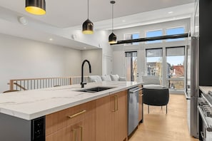 A modern kitchen with a marble countertop, a black faucet, and a built-in dishwasher. - Ember House | Lux 2 Bed | Min to DT (Calgary)
