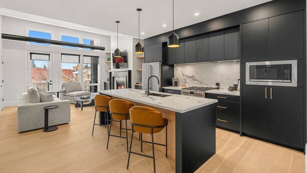 A modern kitchen with a central island, black cabinets, and a large window. - Ember House | Lux 2 Bed | Min to DT (Calgary)
