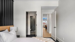 A hotel room with a bed, a nightstand, a bathroom with a shower, and a view of the dining area. - Ember House | Lux 2 Bed | Min to DT (Calgary)