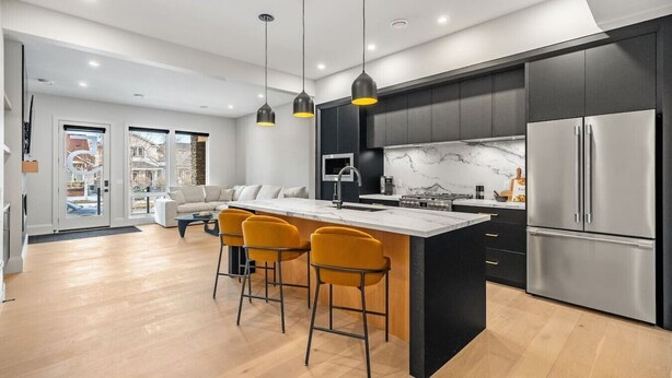 A modern kitchen with a central island, black cabinets, stainless steel appliances, and yellow bar stools. - Onyx Escape | Lux 2 Bed | Garage | Min to DT (Calgary)