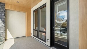 A modern exterior with a wooden ceiling, a stone wall, and a glass door leading to a balcony. - Onyx Escape | Lux 2 Bed | Garage | Min to DT (Calgary)