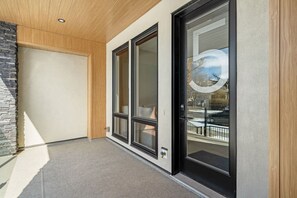 Ein modernes Äußeres mit Holzbalkendecke, Steinwand und Glastür zum Balkon.